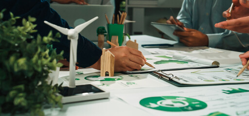 A vibrant workplace scene showcasing a collaborative meeting focused on sustainable strategies, with hands actively engaging with charts and eco-friendly models on the table. SACTR