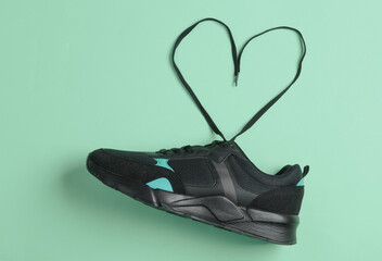 Black sports sneaker with heart-shaped laces on mint green background