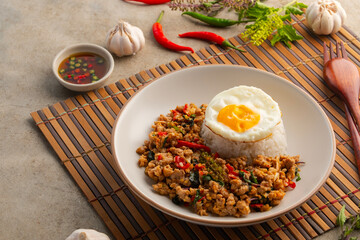 Stie fried minced pork and thai basil with cooked jasmine rice topped with fried egg in white plate.