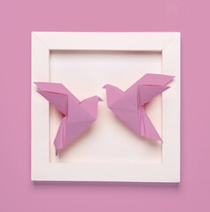 Origami doves in white square frame, pink background. Aesthetic minimal still life. Conceptual photo. Modern art. Top view