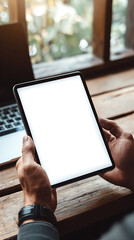 Man holding a blank tablet computer with a laptop and window view in the background hands blank screen
