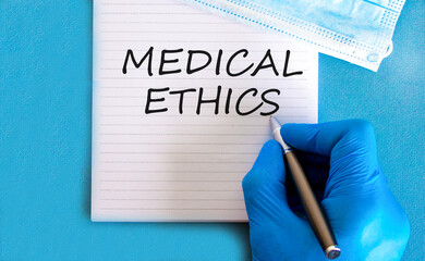 Medical ethics symbol. Concept words Medical ethics on beautiful white note. Doctor's hand in blue...