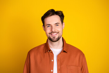 Young man wearing a casual orange shirt smiles confidently on a vibrant yellow background, exuding...
