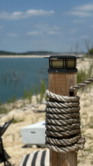 Fototapeta premium Rope-wrapped wooden post by scenic lake shoreline under clear blue sky - concept of travel, tourism, outdoor nature retreats