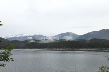 Lake with pine forest and mountains in mist after rain, calm alpine landscape.