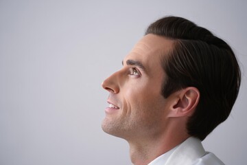 Fototapeta premium Profile view of a man with dark hair looking upwards against a plain light background area