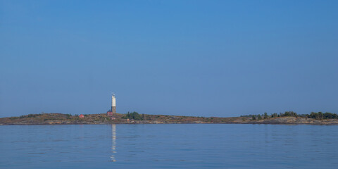 Small lighthouse with adjacent house on rocky islet in the Baltic Sea. Coastal scene in Finland with traditional maritime architecture, peaceful waters, and northern light