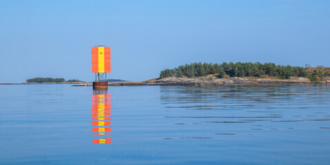 Marine channel marker on coastal rocks forming a leading line toward the horizon in the Baltic Sea on a sunny day. Northern seascape with clear light, perspective, and maritime atmosphere