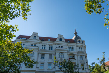 Obraz premium Majestic residential building with a domed tower and a classic facade. Green foliage frames the scene.