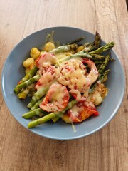 Delicious gnocchi dish with asparagus and tomatoes topped with melted cheese on a blue plate