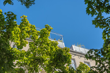 Roof terraces with glass railings and fairy lights, framed by green treetops. Summery urban scene.