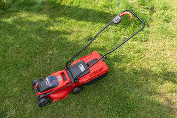 Top view of a red lawn mower standing on freshly cut green grass. Handle and controls are clearly visible.