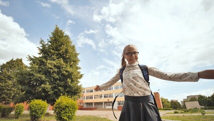 Happy schoolgirl spinning with open arms in front of school building, enjoying the end of school...