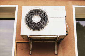 Old air conditioning unit installed outside on building wall. Dirty ventilation system with metal...