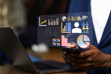 African business executive managing business operations across multiple devices, synchronizing real-time financial data and analytics between a smartphone and laptop.