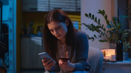 Caucasian woman holding mobile phone sad upset girl drink wine at home night worried bad news...