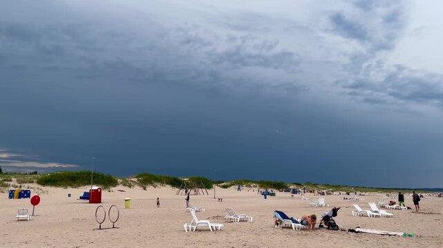 Before the storm: beachgoers at Ventspils shore under heavy summer sky in dramatic contrast