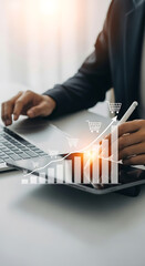 Person using laptop and tablet to analyze sales growth chart with shopping cart icons graph business