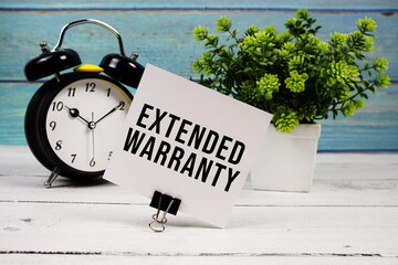 Extended Warranty text written on paper card with alarm clock on wooden background