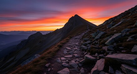 Fototapeta premium A winding mountain trail leading to a peak under a vibrant sunset with orange and purple hues in sky