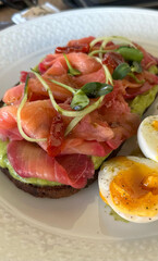 Delicious avocado toast with smoked salmon and soft-boiled egg on white plate - concept of gourmet meals for restaurants and cafes