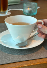Female hand holding cup of tea on cozy café table with tealight candle - concept of relaxation in hospitality and cafés