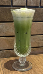 Refreshing iced matcha latte in elegant glass against brick wall for cafe, bistro, and tea bar concept