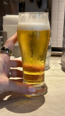 Female hand holding chilled beer glass in modern bar setting for breweries and pubs concept of...