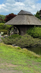 Rustic watermill by tranquil pond in lush countryside landscape with clear sky concept of travel agency or eco-tourism ads