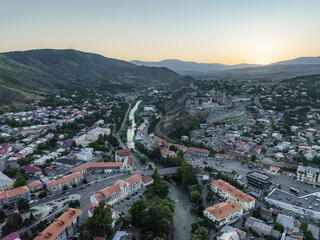 Aerial view of the imposing Rabati Castle standing sentinel over the winding river and terracotta rooftops under a golden sky, Akhaltsikhe, Samtskhe-Javakheti, Georgia.