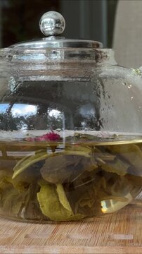 Steaming herbal tea leaves slowly unfurling in glass teapot