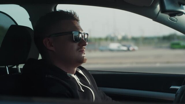 Young bearded man in sunglasses sits in the car, tries to steal it and turn it on without keys, nothing works out, he is caught on the crime scene. Carjacker, crossing the boundaries of law.