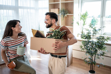 Happy couple carrying boxes and plants into new home