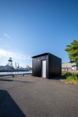 Fototapeta premium A sleek, modern black structure is prominently positioned along the waterfront, basking in the bright sunlight of a clear blue sky. This bustling port is alive with the activity of cranes and ships.