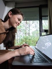 Young woman smiling while using a laptop in a cozy home environment, showcasing a relaxed and...