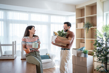 Happy couple carrying boxes and plants into new home
