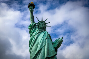 Fototapeta premium Iconic Statue of Liberty holding torch and tablet rising against a dramatic cloudy sky on Liberty Island