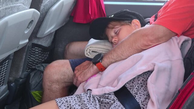 Sleepy child rides on bus with father. Little girl sleeps in the passenger seat. Dad sitting nearby.