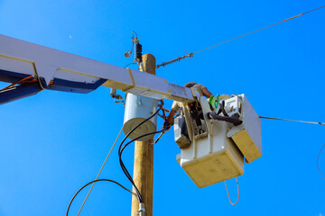 Electrical technicians in bucket lift conduct maintenance on utility pole under bright blue sky.