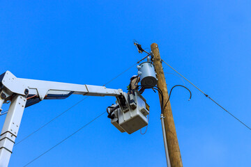 Utility electrical worker uses bucket truck to fix an electrical transformer atop wooden pole...