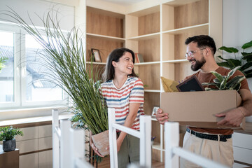 Happy couple carrying boxes and plants into new home