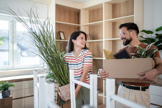 Happy couple carrying boxes and plants into new home
