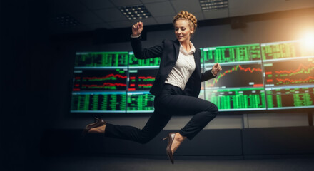 Successful businesswoman jumping for joy in front of stock market data screens. Happy female trader celebrating financial profit and growth.