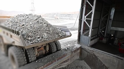 Quarry dump truck unloads ore for crushing, processing plant open pit mine.