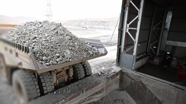 Quarry dump truck unloads ore for crushing, processing plant open pit mine.