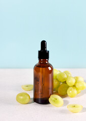 Grape seed oil in dropper bottle with fresh green grapes on a blue background. Skin care concept.