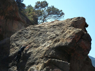 Young climber and hiker free-climbing on sunny spring day at Sa Foradada beach, Deià, Serra de...