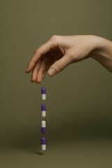 Fototapeta premium Hand releasing purple-white capsules against neutral background
