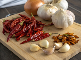 Dried red chilies, garlic, and onion on a wooden cutting board