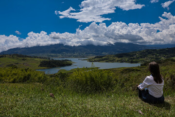 Female tourist sitting looking at the biggest artificial lake in Colombia called Calima Lake located on the mountains of Darien at the region of Valle del Cauca